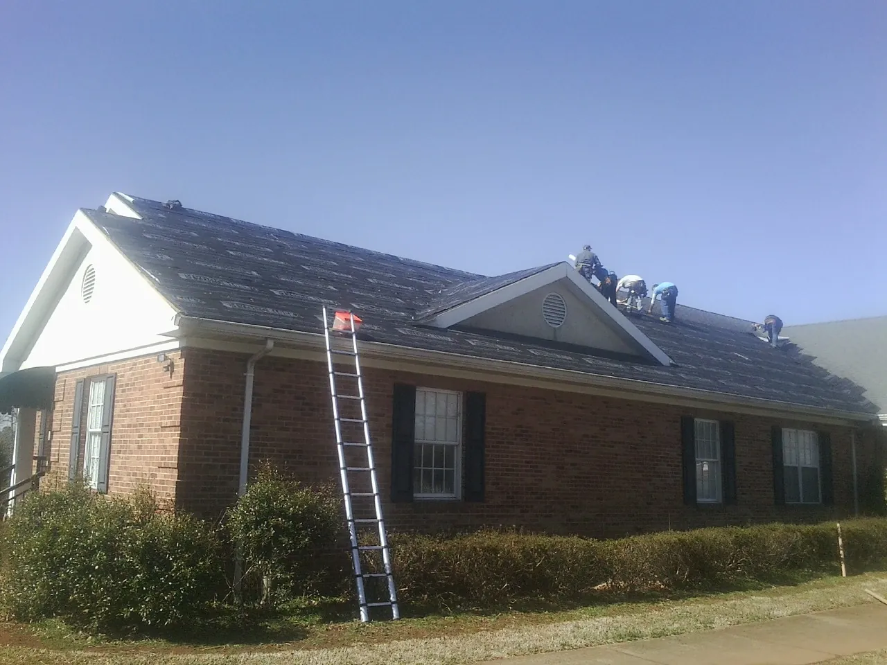 Crew tearing shingles off a brick ranch roof with a ladder set — Emergency Roof Repair work by our crew in Bridgewater